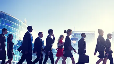 A group of professionals walking across a road with city buildings in the background.